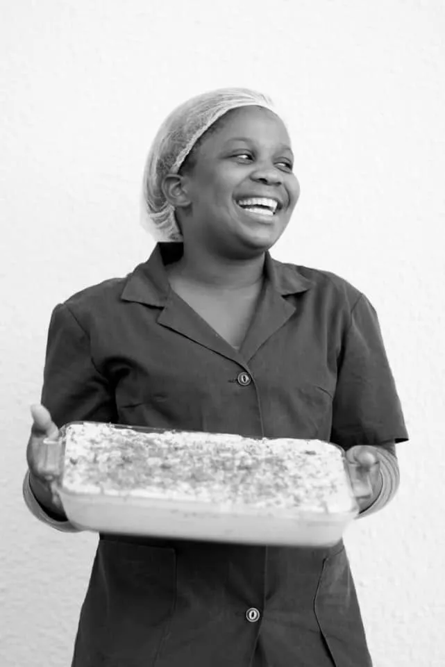 A laughing member of the kitchen team carrying a tray of dessert